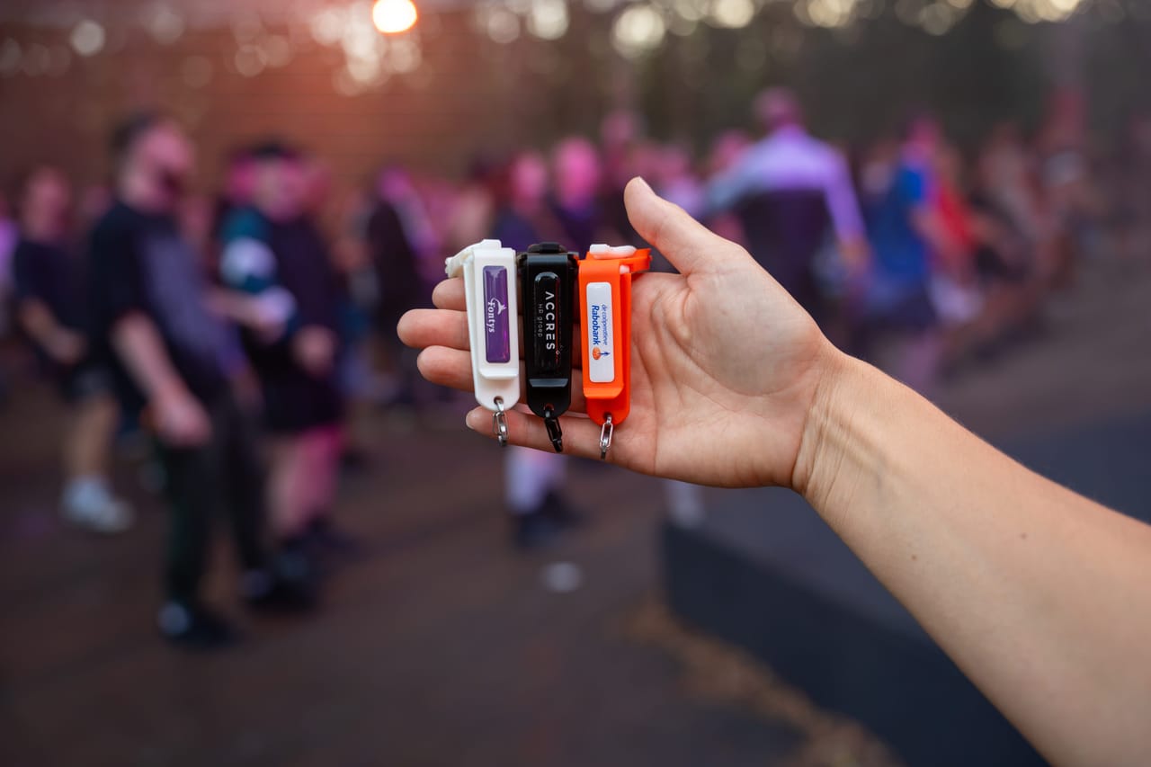 A hand holds up Mr Clipr in white, black and orange in front of a festival crowd at sunset
