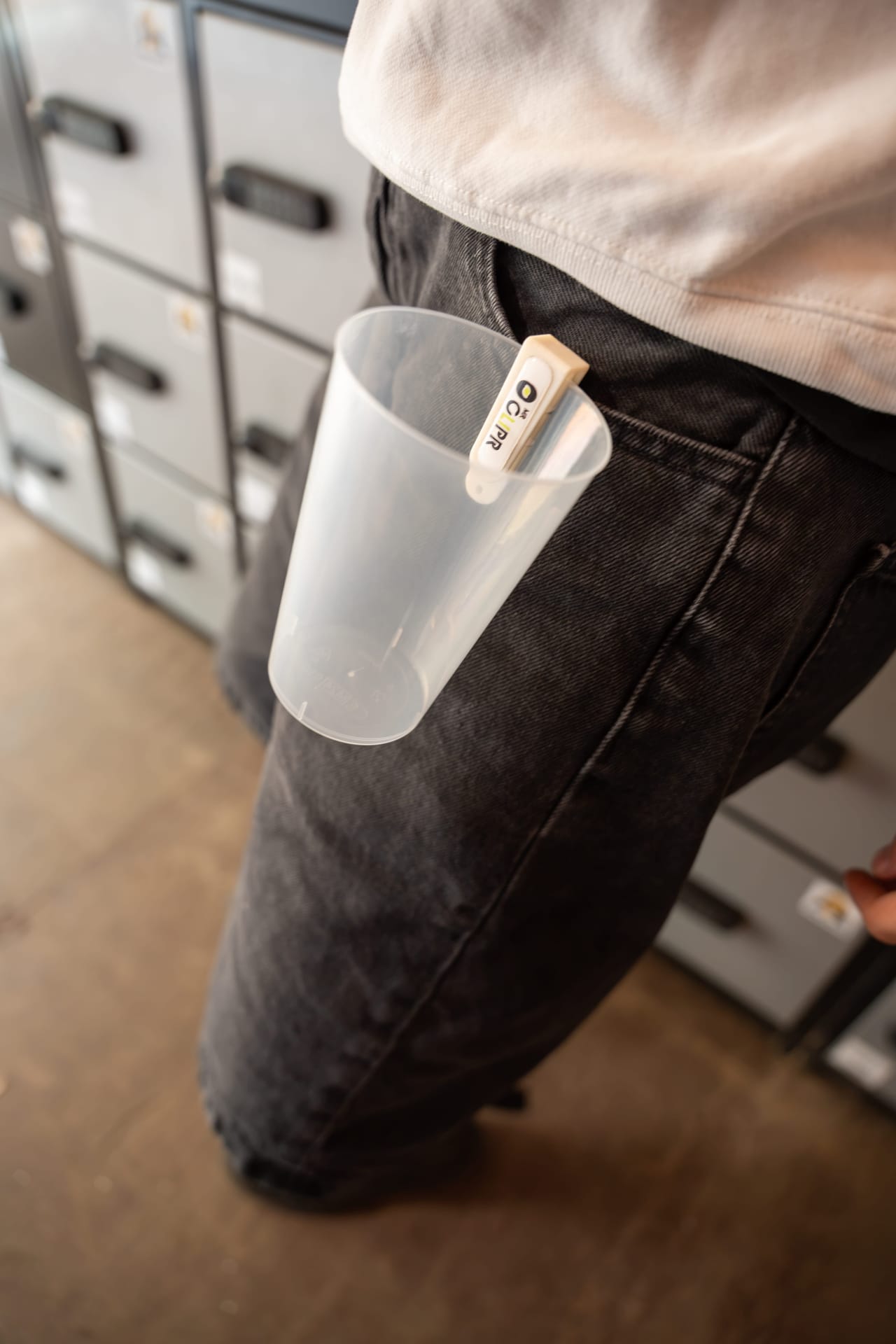 Witte Mr Clipr aan een jeans met een beker, bij de lockers