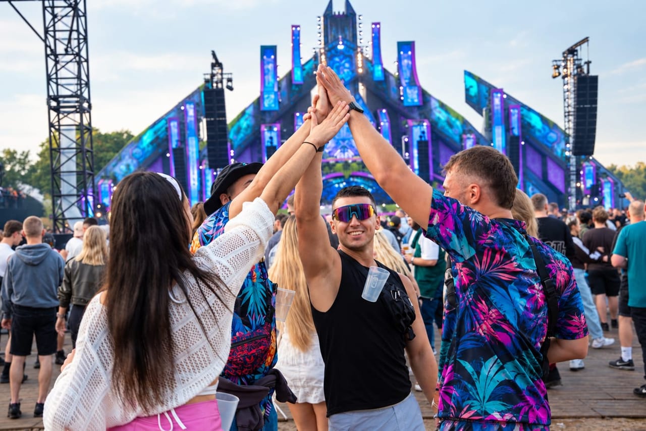 Friends high-fiving in front of the main stage, cups hanging from their Mr Clipr